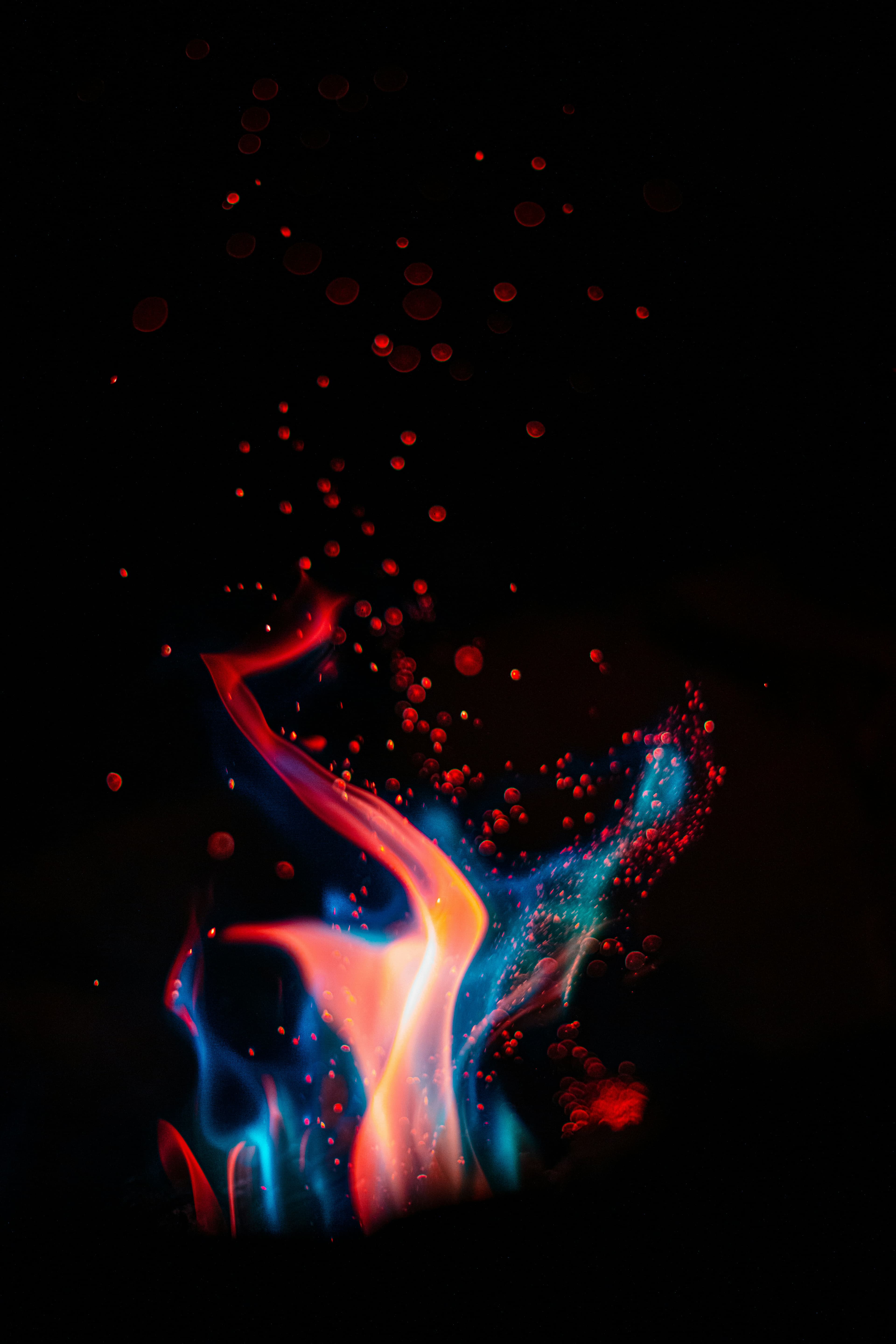 A flame burning red and blue against the dark, embers rising